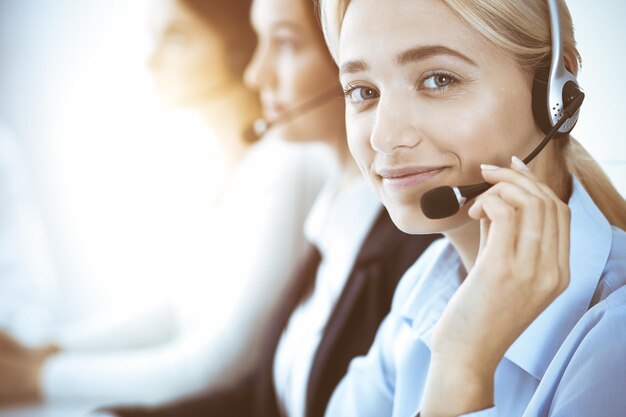 Photo call center and business people concept beautiful business woman with headphones consulting clients group of diverse phone operators at work in office