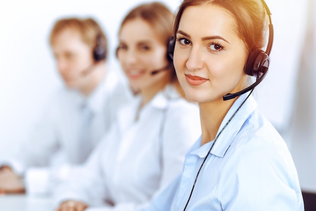 Call center operators. Focus on beautiful business woman using headset in sunny office.