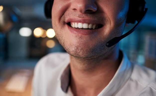 Call center smile and mouth of a worker in telemarketing support and crm business in a dark office Ecommerce contact us and happy customer service agent with a headset during night shift