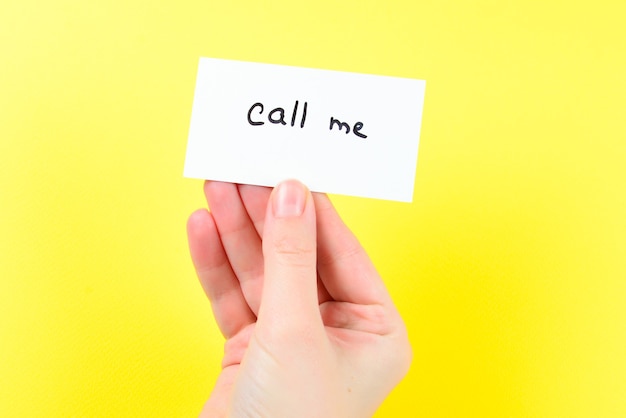 Call me text on a card in woman hand  on a yellow surface.