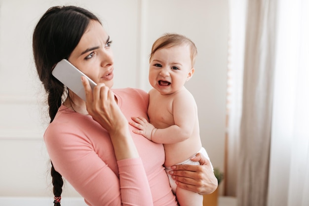 Call to pediatrician worried young mother upset of crying baby talking on phone with doctor and