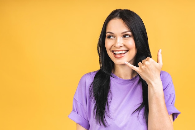 Call sign Portrait of happy smiling brunette girl in casual isolated over yellow background