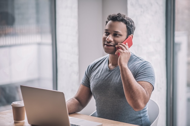 On the call. Young businessman sitting at the table in the office and talking on the phone