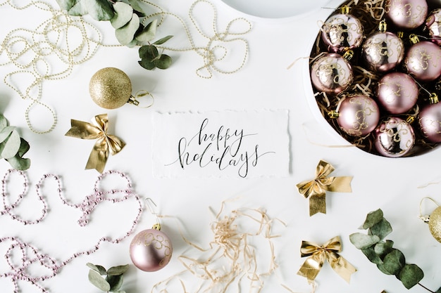 Calligraphy words happy holidays and frame made of christmas decoration with christmas balls, tinsel, bow, eucalyptus.