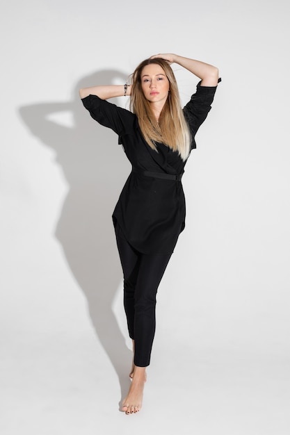 Calm attractive blonde woman in a black suit standing barefooted and touching her hair.