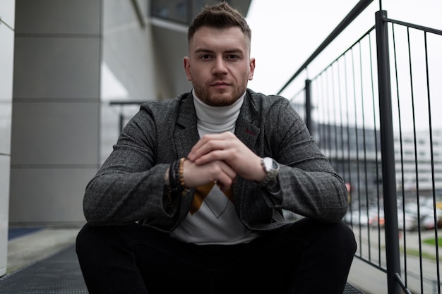 Calm balanced brutal man sits with his hands clasped in the lock and looks at the camera