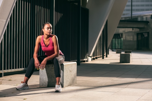 Calm beautiful sportswoman sitting on the granite cube and looking away. Template banner