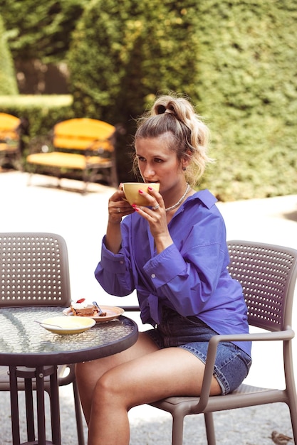 Calm beautiful young woman sits in street cafe and drinking some coffee in cup with good summer mood Looking for someone and waiting for meet