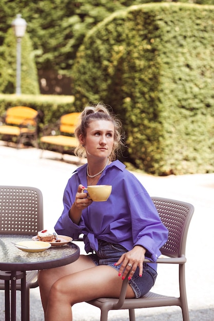 Calm beautiful young woman sits in street cafe and drinking some coffee in cup with good summer mood Looking for someone and waiting for meet