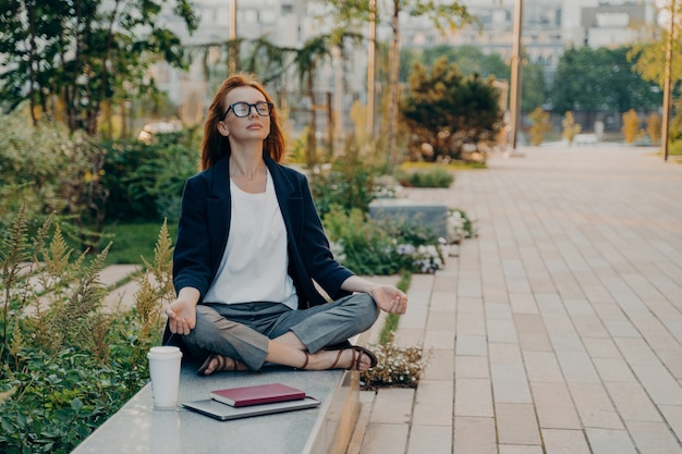 Calm business woman meditating in lotus outdoors peaceful female freelance employee practicing yoga