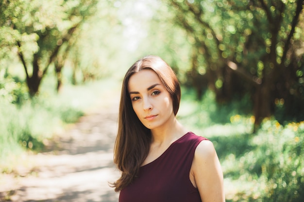 Calm gorgeous young brunette woman in a stylish dress is walking and posing in the summer garden.