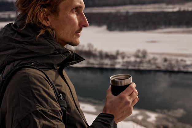 Calm male walking in snowy forest in winter drinking teaLocal travel exploring nature