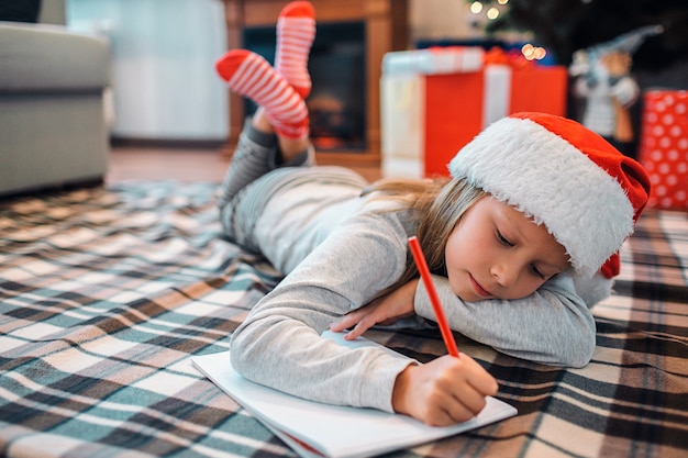 Calm and peaceful girl lying on floor and writing letter. 