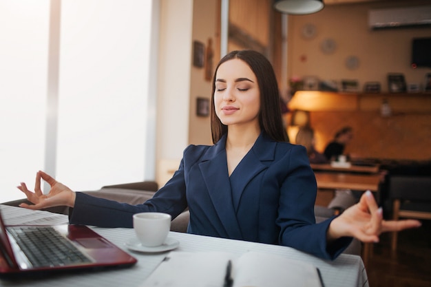 Calm and peaceful young woman sit on table and meditation