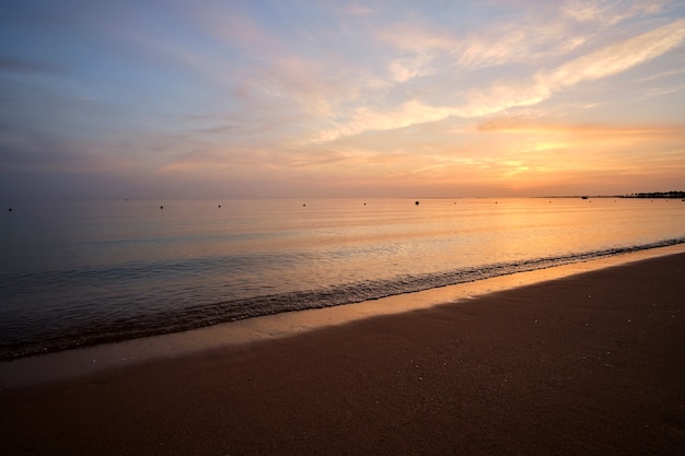 Calm sea shore with crushing waves on sandy beach at sunrise.