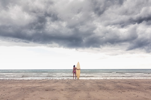 Calm woman in bikini with surfboard on beach