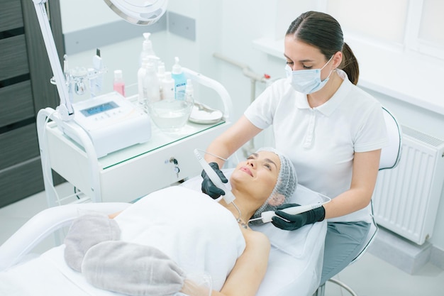 Calm young lady during the paraffin therapy of hands and micro current stimulation of neck skin