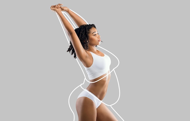 Calm young slim african american woman in white lingerie enjoys weight loss result with fat abstract body around