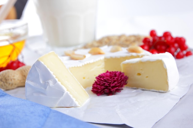 Camembert nuts berries and biscuits with seeds on white parchment paper Cheese with honey a glass of milk and a blue and white napkin on a light background Closeup