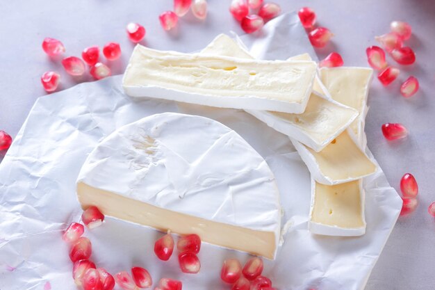 Camembert and pomegranate seeds on parchment paper on a light background Delicious cheese on the table closeup A great product for a breakfast