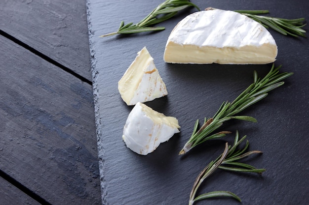 Photo camembert and rosemary on slate board soft cheese with white mold on dark background camembert