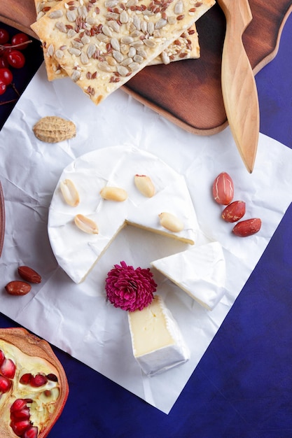 Camembert with nuts and berries on white parchment paper Closeup of cheese with a pink flower on a blue background