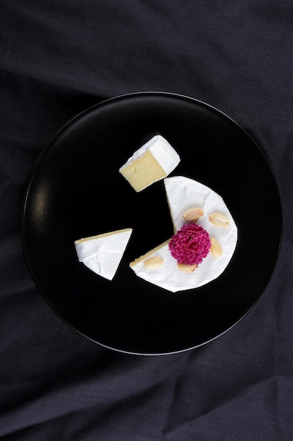 Camembert with nuts and a rose flower on a black plate Closeup of cheese on a black background View from above