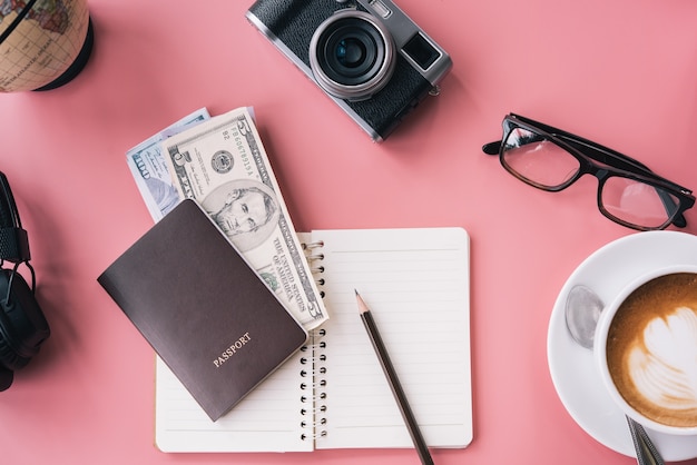 Camera, glasses, headphone and notepad on pink background, Travel Planner concept.