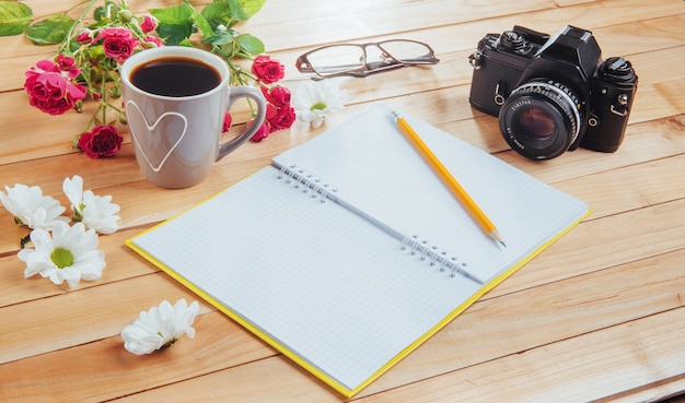 Camera, glasses and notepad and pencil on a brown wooden 