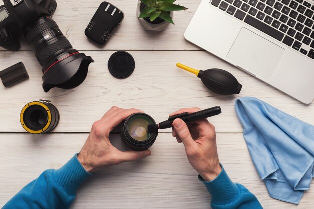 Photo camera lens cleaning with special brush, close-up. photographer hands sweeping lens on workplace . professional photographing equipment care, technology concept