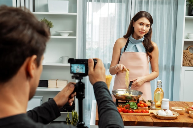 Cameraman recording to woman in chef influencer cooking spaghetti postulate