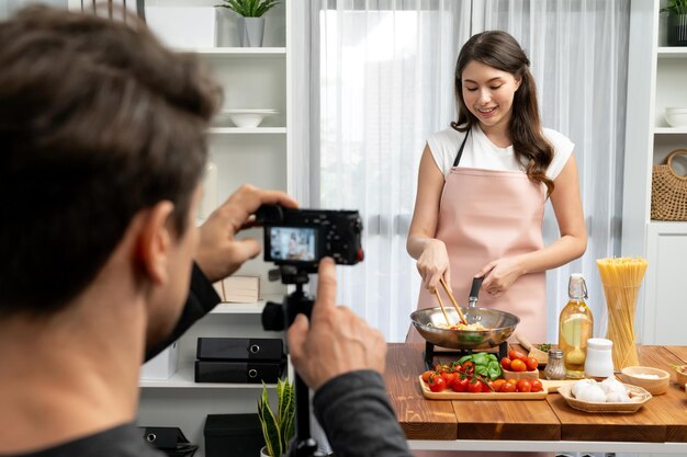 Cameraman recording to woman in chef influencer cooking spaghetti postulate