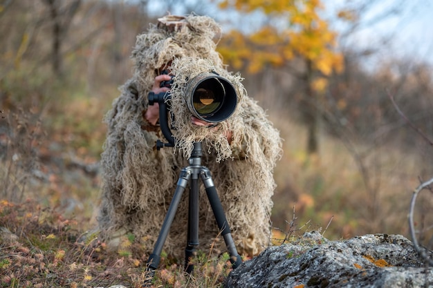 Camouflage wildlife photographer in the ghillie suit working in the wild