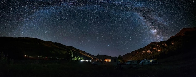 Camper van under panoramic night sky in the Alps The Milky Way galaxy arc and stars over illuminated motorhome Camping freedom in unique landscape