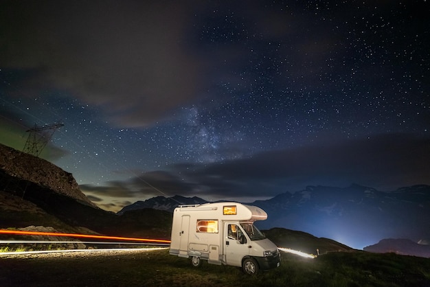 Camper van under panoramic night sky in the Alps The Milky Way galaxy arc and stars over illuminated motorhome Camping freedom in unique landscape