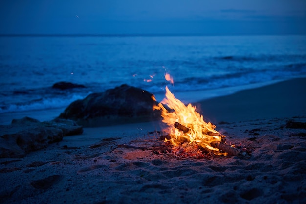 A campfire burns on a deserted sandy beach at the seashore in the evening