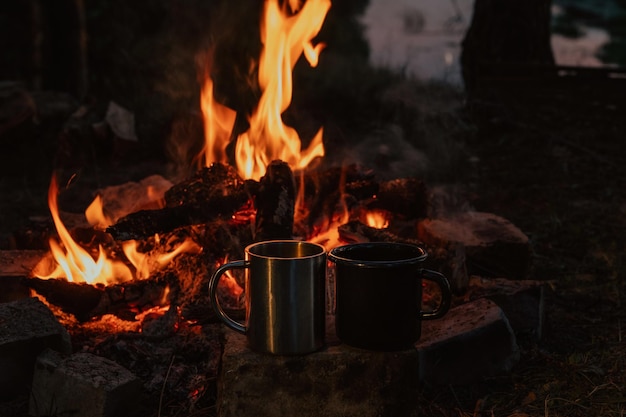 Camping cups two pieces against the background of a campfire closeup flames charred pieces of logs Landscape Camping