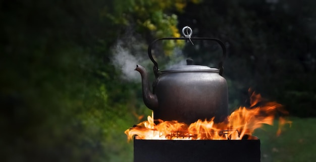 Camping kettle boiling on the grill and steam coming from the spout against the backdrop of nature