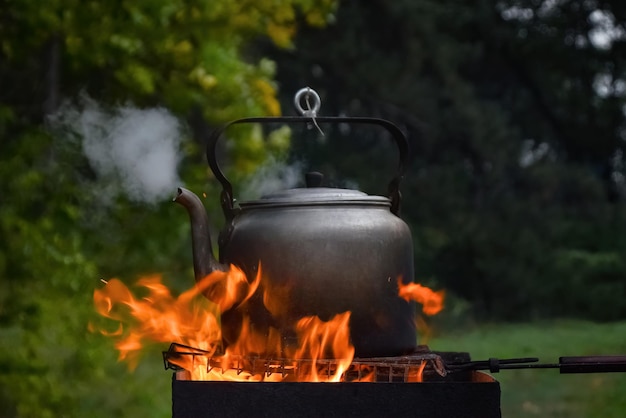 Camping kettle boiling on the grill with steam from the spout on the background of natural nature