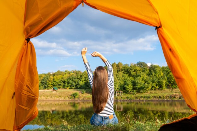 Camping on lake shore at sunset, view from inside tourist tent. Girl enjoy nature in front of tent