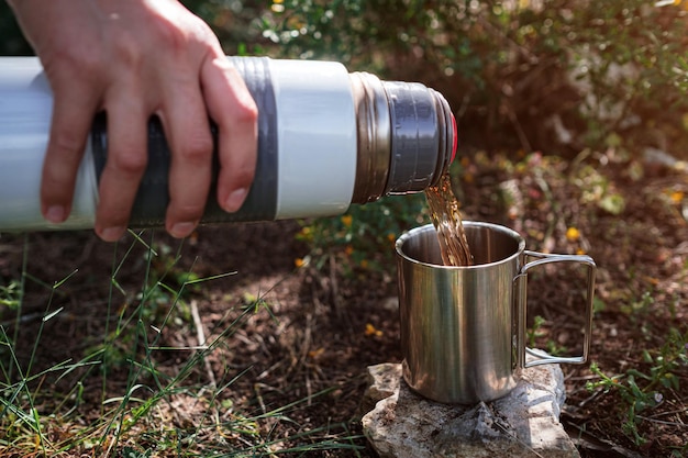 In a camping mug pours tea from a thermos in nature