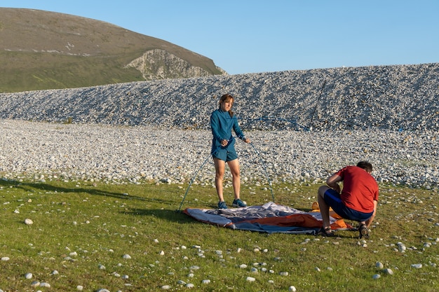 Camping people outdoor lifestyle couple putting up a tent in nature rocky beach