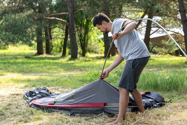 Camping, travel, tourism, hike concept - young man setting up tent outdoors.