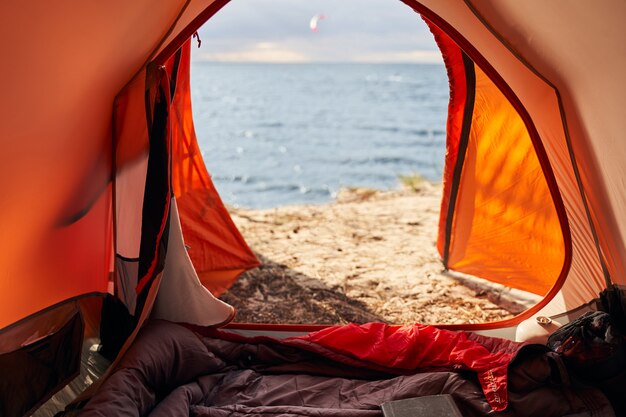 Camping with sleeping bag is situated with door coming out on beach and waves in nature