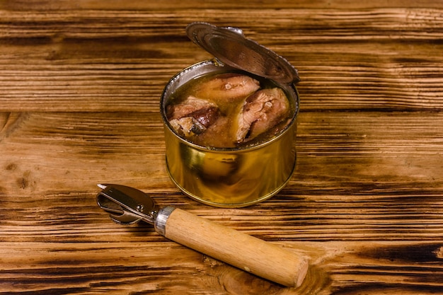 Can opener and tin can with sardine on wooden table