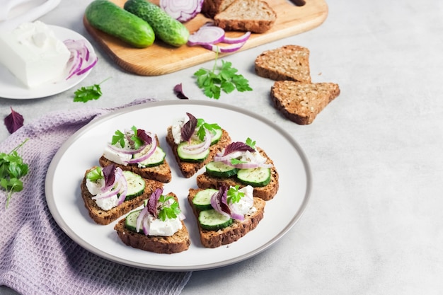 Canapes with toasted bread with sunflower and flax seeds, feta cheese, cucumber and onion