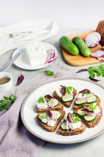 Canapes with toasted bread with sunflower and flax seeds, feta cheese, cucumber and onion