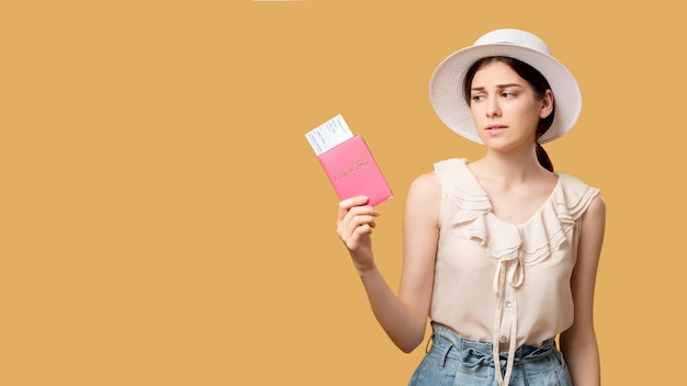 Canceled vacation Travel ban Delayed flight Holiday tour Disappointment regret Sad woman summer outfit looking at foreign passport tickets isolated on beige copy space