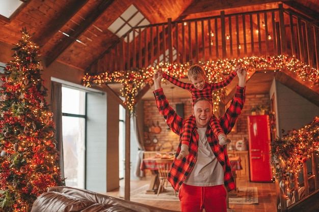 Candid authentic happy dad and son in red plaid pajamas fooling around at wood lodge Xmas decorated