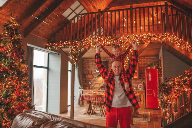 Candid authentic happy dad and son in red plaid pajamas fooling around at wood lodge Xmas decorated